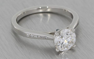 Platinum solitaire engagement ring set with a round brilliant diamond and channel set shoulders